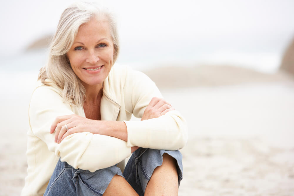 Oudere vrouw zittend op het strand, had urineverlies na een heupoperatie